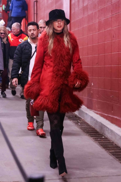 Taylor Swift bundled up in a Chiefs-red winter coat and a black fuzzy bucket hat to cheer on Travis Kelce at the Chiefs vs. Texans game on Saturday, December 21. See her game-day outfit, here.